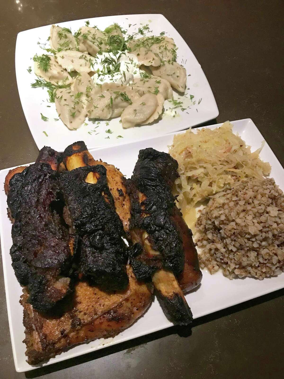 A barbecue plate from Web House Café & Bar included three ribs, two chicken leg quarters, a smoked sausage, and sides of sauerkraut and buckwheat.  In the back is an order of potato and dill vareniki.