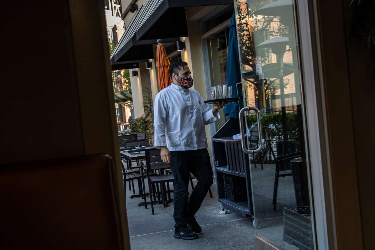 Axel Gomez, a server at MoMo's Bar & Grill, is seen with a mask in San Francisco in November. California announced that it was reinstating its requirement for universal indoor masking.