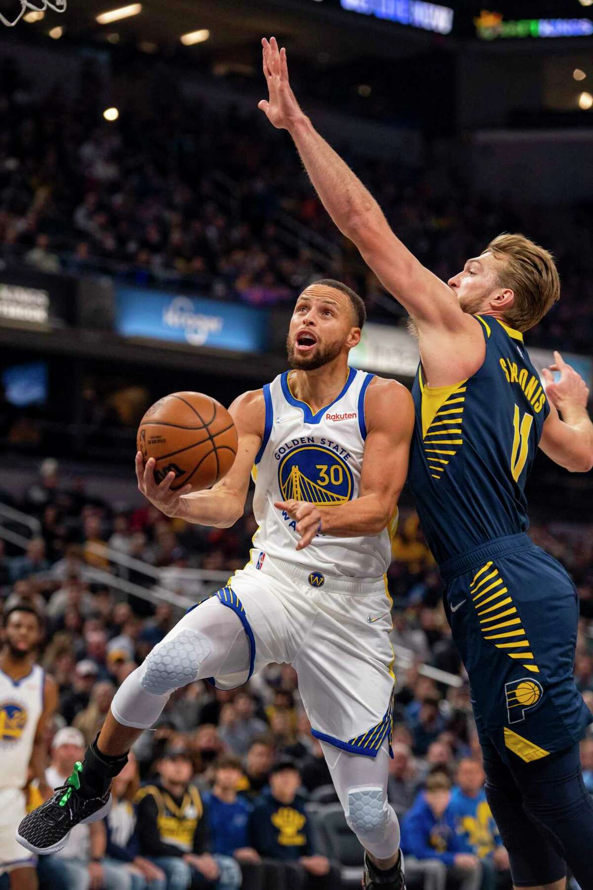 Golden State Warriors guard Stephen Curry (30) slips under the defense of Indiana Pacers forward Domantas Sabonis (11) for a scoring attempt during the first half of an NBA basketball game in Indianapolis, Monday, Dec. 13, 2021. (AP Photo/Doug McSchooler)