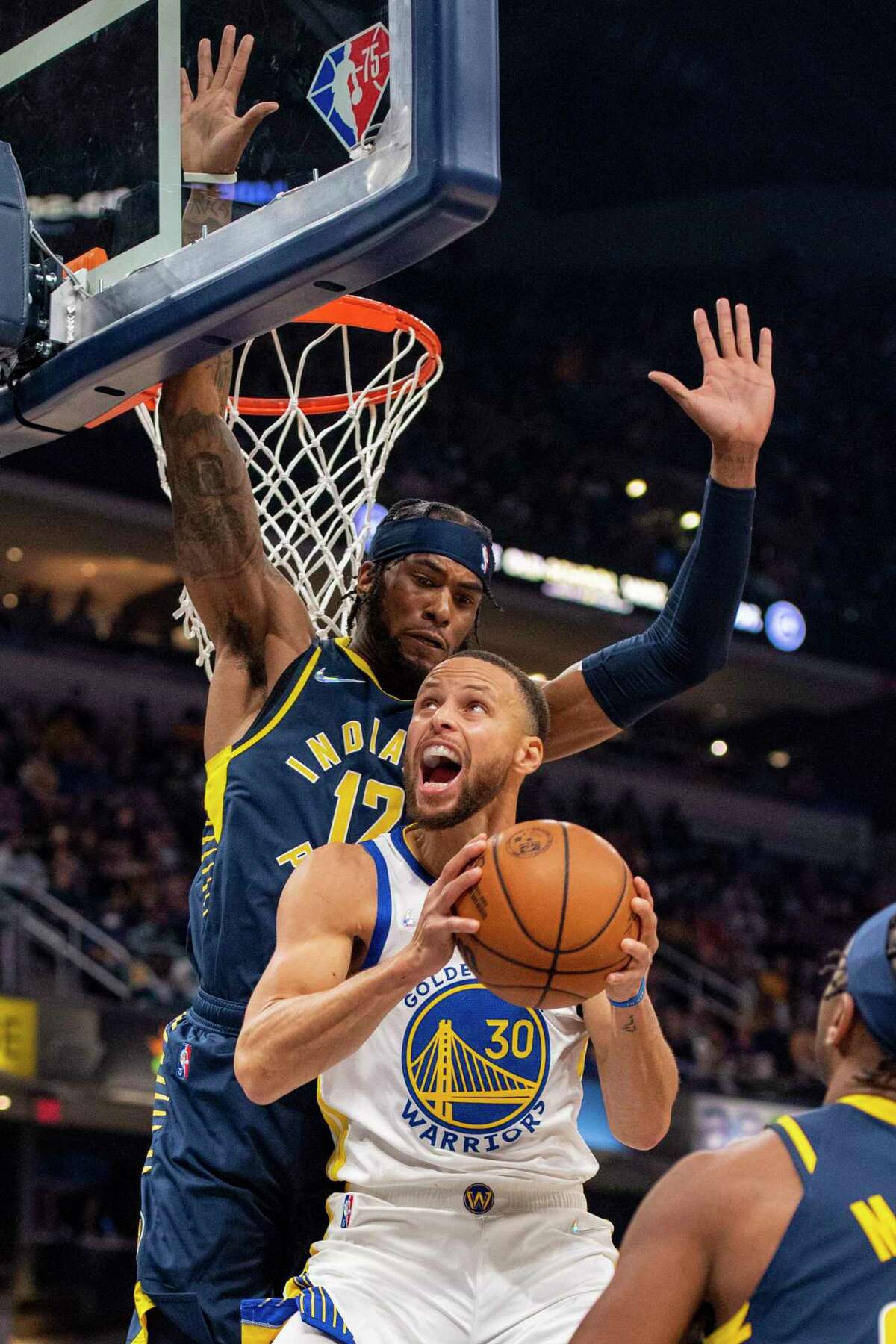 Indiana Pacers forward Oshae Brissett (12) works to stop a scoring effort by Golden State Warriors guard Stephen Curry (30) during the first half of an NBA basketball game in Indianapolis, Monday, Dec. 13, 2021. (AP Photo/Doug McSchooler)