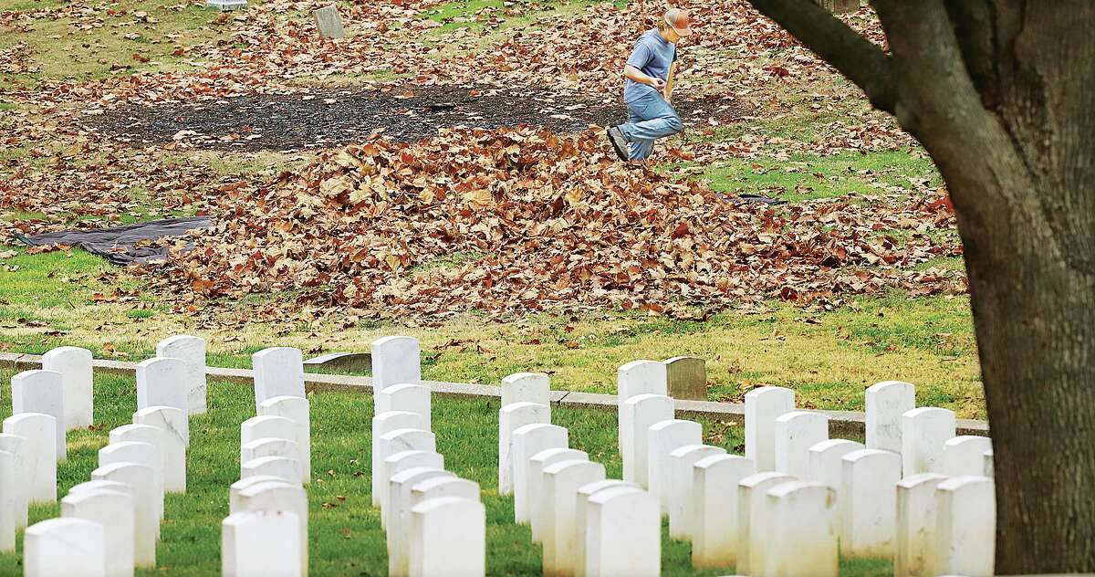 John Badman|The Telegraph A worker rakes up a big pile of leaves on the Alton City Cemetery property Tuesday, adjacent to the Alton National Cemetery, foreground. Several workers were raking, blowing, mowing and burning leaves and fallen branches in the City Cemetery. The Alton National Cemetery, at 600 Pearl St., will host the Wreaths Across America ceremony Saturday, Dec. 18, at 11 a.m. The graves will be decorated with Christmas wreaths to honor the deceased veterans. Wreaths Across America began with just a section of Arlington National Cemetery being decorated with wreaths in 1992. By 2005 it was a national event and today hundreds of thousands of wreaths are placed on the graves of veterans in more than 1,000 locations across the United States.