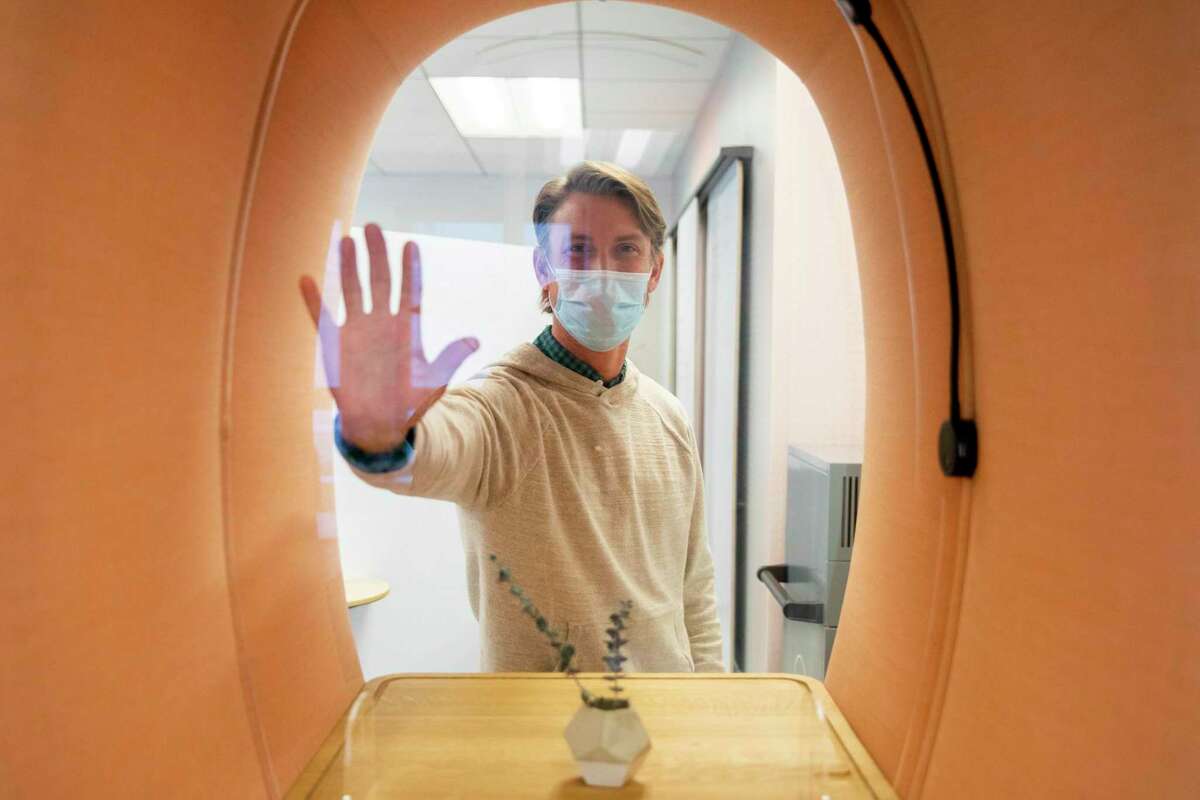Brandon Cook places his hand on a plexiglass barrier at a standing desk at Workplace 2030 in San Francisco. San Francisco offices where everyone is fully vaccinated will not have to return to masking.