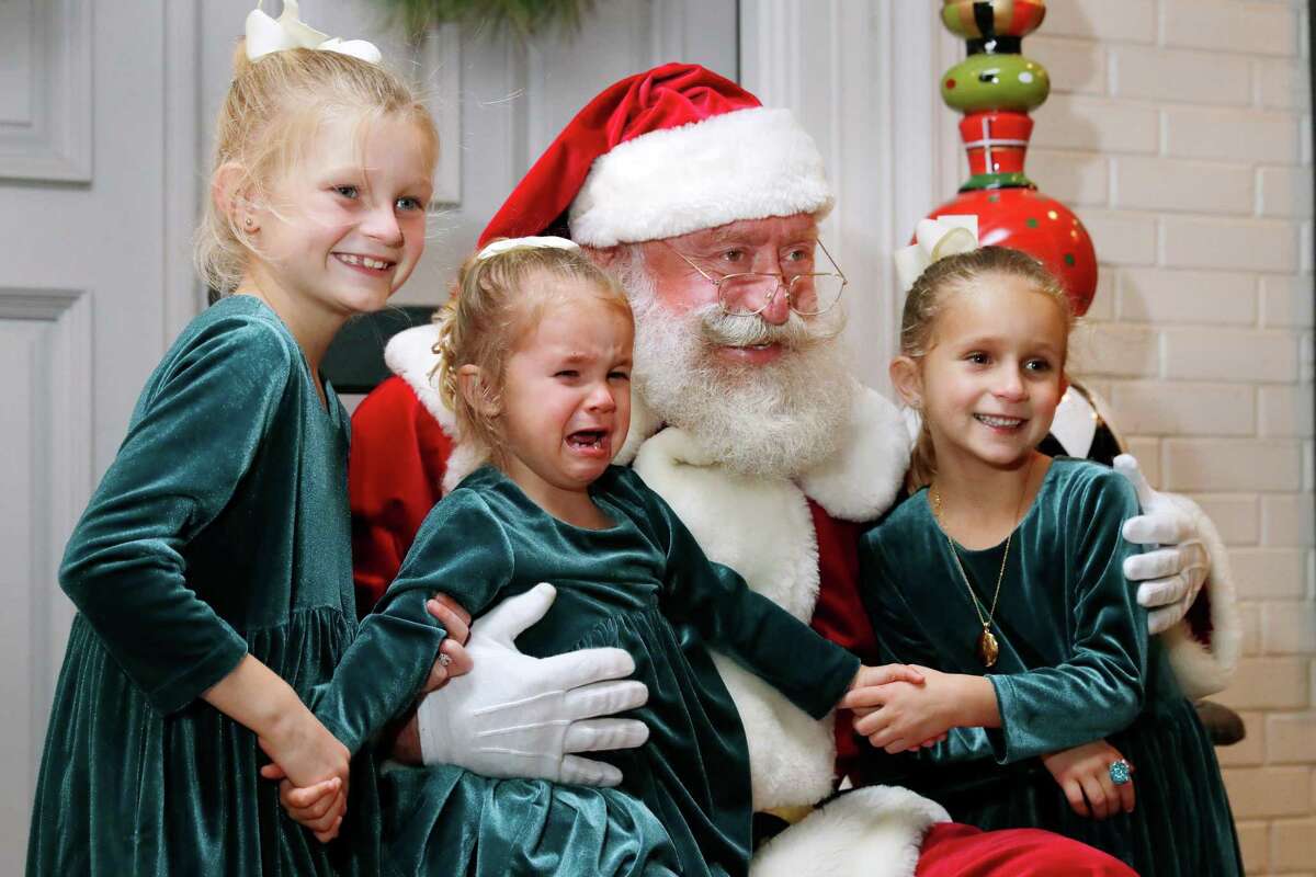 Gordon Taylor, as Santa, sits for a photo with the Van Burkleo sisters, from left, Adeline, age eight, Charlotte, age two, and Genevieve, age six, during a block party on Latexo Dr. Friday, Dec. 10, 2021 in Houston, TX.