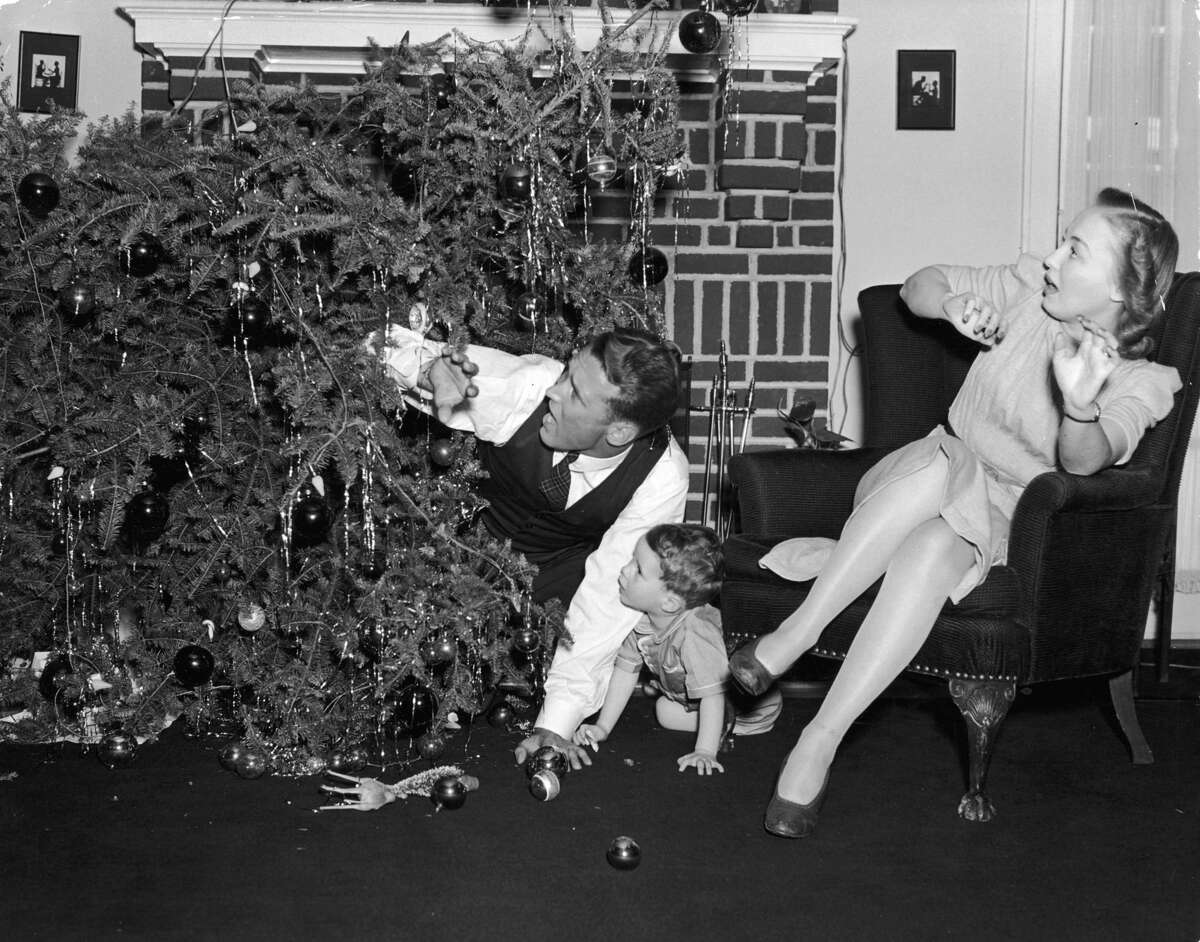 Circa 1945: A family recoils after their Christmas tree toppled over in front of their fireplace. The father and son crouch on the floor while the mother sits in an armchair. Several ornaments lie on the floor. (Photo by Lambert/Getty Images)