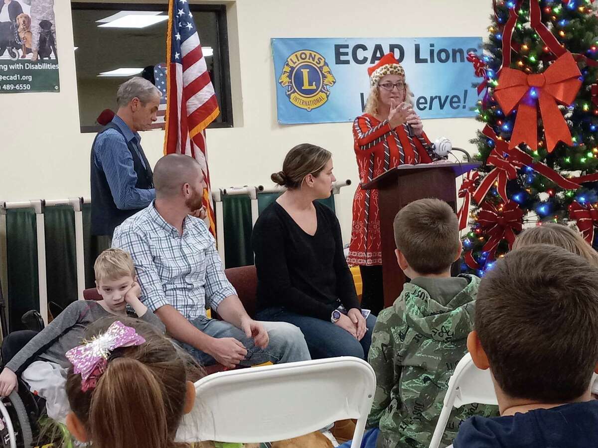 Educated Canines Assisting with Disabilities, or ECAD, held graduation ceremonies for three families Wednesday night at the dog training facility in Winchester. Pictured is Lu Picard, standing at the podium, and her husband, Dale, left; seated, from left, are Luke Canniff, 6, and his parents, Tim and Lisa. Luke, who is paralyzed from the waist down, was paired with a golden retriever named Melon.