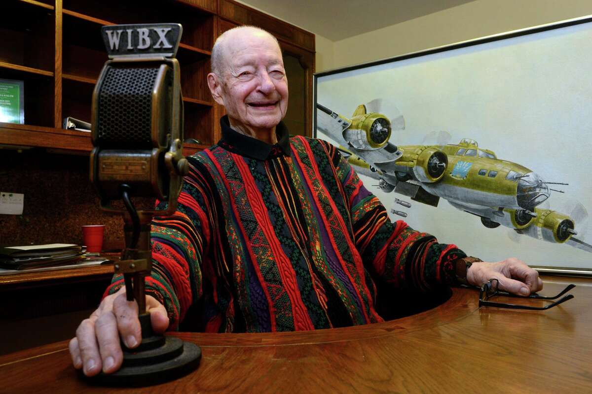 Frank Boyle poses in his home in Shelton, Conn. Dec. 16, 2021. Boyle, a World War II veteran, has also recently honored for his career in radio broadcasting. Boyle is seen here with vintage broadcast microphone from WIBX, in Utica, New York and a painting of a Boeing B-17 Flying Fortress. Boyle served as a ball turret gunner, flying in B-17 bombers over Europe in the second world war.