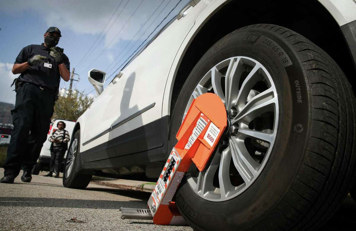 Omar Nicholson, a parking compliance officer, demonstrates a new boot system Thursday, Dec. 9, 2021, near the intersection of St. Emanuel Street and McKinney Street in Houston. The new boot can be paid for and unlocked remotely.