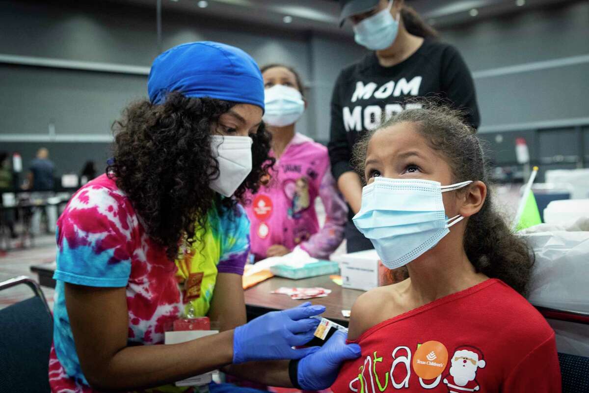 Evelyn Mayfield, 8, looks up as she receives a COVID-19 vaccination from Staysha Hampton, LVN, during a city-wide vaccination clinic at the George R. Brown Convention Center Friday, Dec. 17, 2021 in Houston. Texas Children’s Hospital and the City of Houston hosted a free citywide COVID-19 vaccine clinic for attendees aged 5 and older. Eligible participants were able to receive first or second doses of the Pfizer or Moderna vaccine, or an additional dose of the Pfizer or Moderna vaccine, or a booster dose of the Pfizer or Moderna vaccine, as needed.