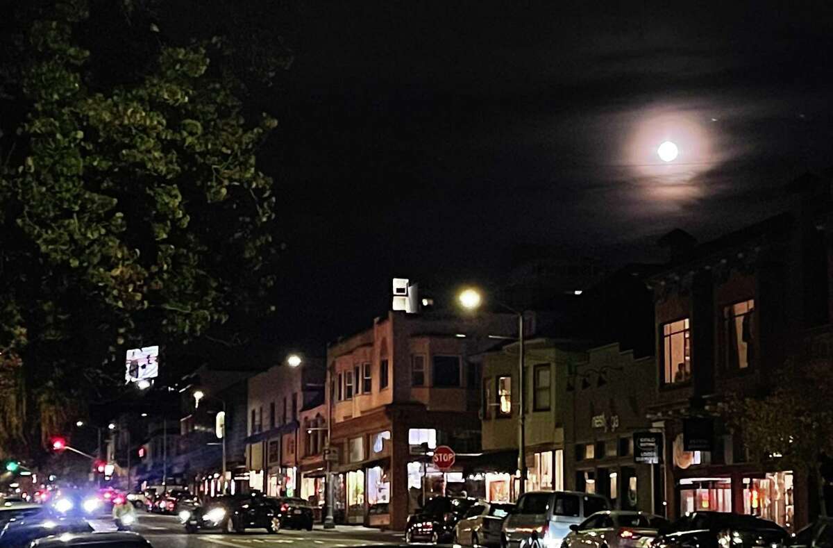 The last full moon of 2021, known as a “cold moon,” rises through the clouds over Piedmont Avenue in Oakland on Saturday.