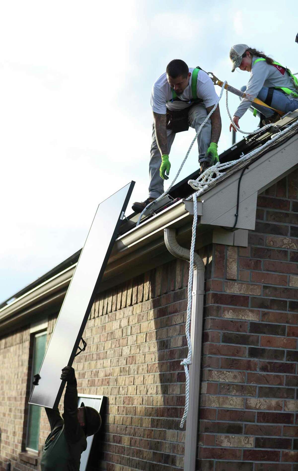 Steven Broussard hands Daniel Molina a solar panel as their team from Texas Solar Outfitters installed solar panels on a home, Friday, Dec. 17, 2021 in Cypress.