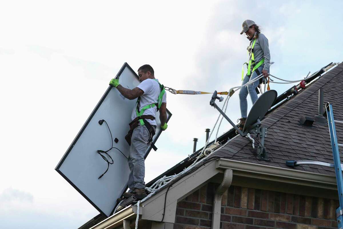 Daniel Molina moves a solar panel with Laura Masterson as their team from Texas Solar Outfitters, installed solar panels on a home, Friday, Dec. 17, 2021 in Cypress. Under the city’s newly adopted building code, many new homes will have to be solar-ready.