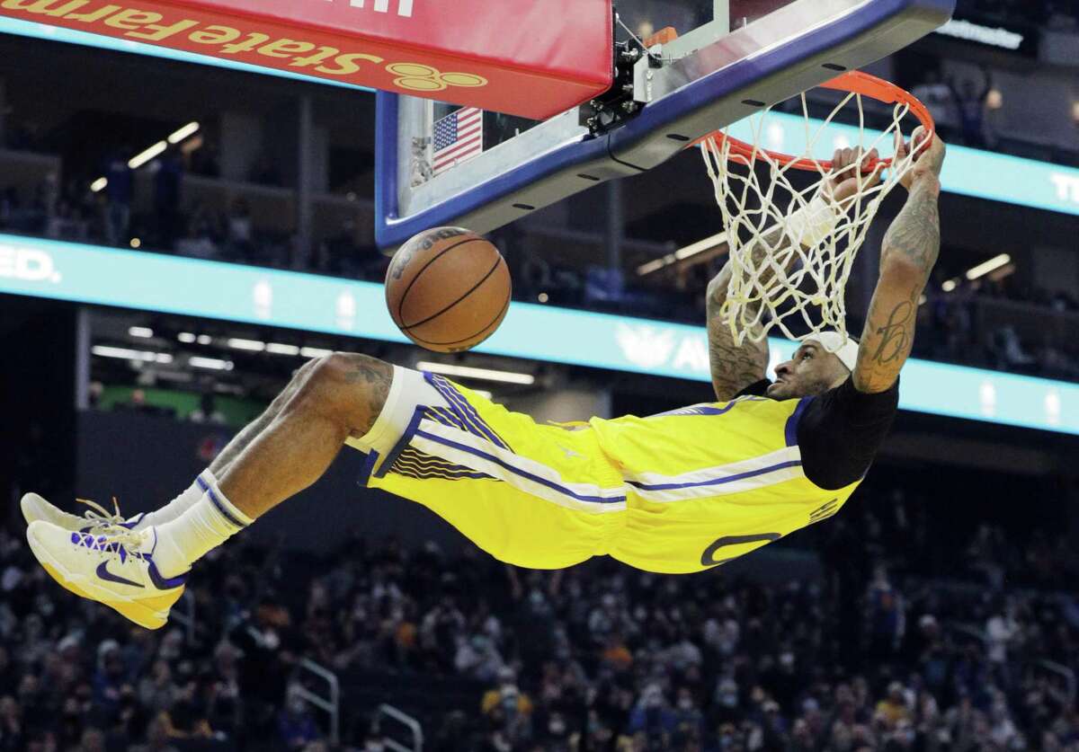 Gary Payton II (0) hangs from the basket after a steal and dunk in the first half as the Golden State Warriors played the Sacramento Kings at Chase Center in San Francisco, Calif., on Monday, December 20, 2021.