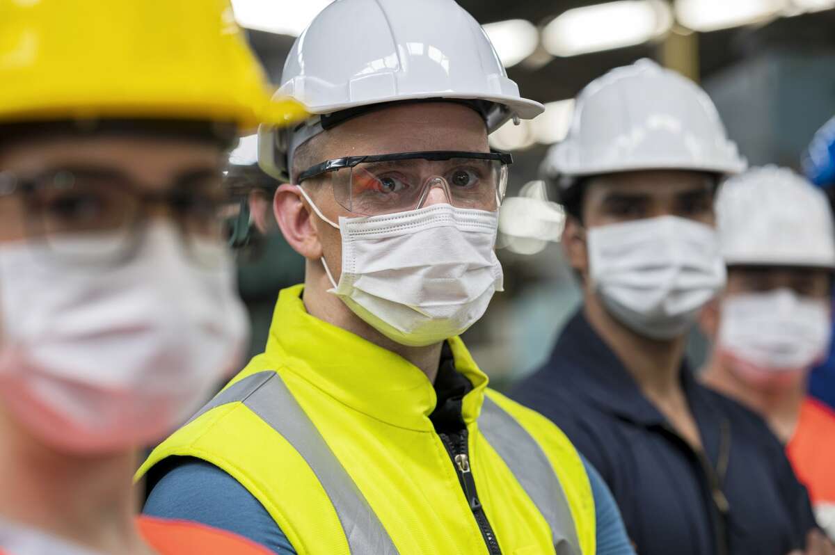 Shot of Business owner smiling under protective face mask while standing side by side with working team in a heavy industry.