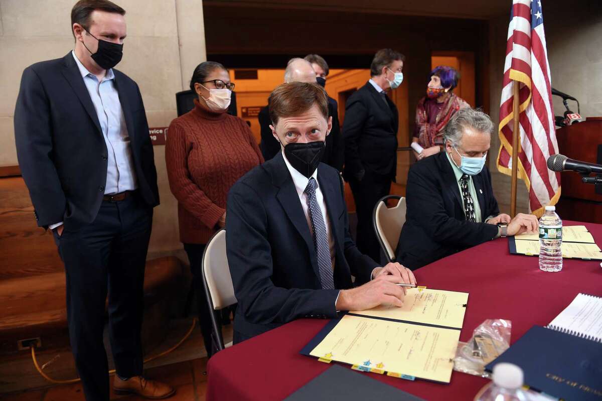 U.S. Sen. Chris Murphy, left, watches New Haven Mayor Justin Elicker, center, and state Department of Transportation Commissioner Joseph Giulietti, right, sign a lease for a partnership agreement for Union Station and State Street Station in New Haven Dec. 21, 2021.
