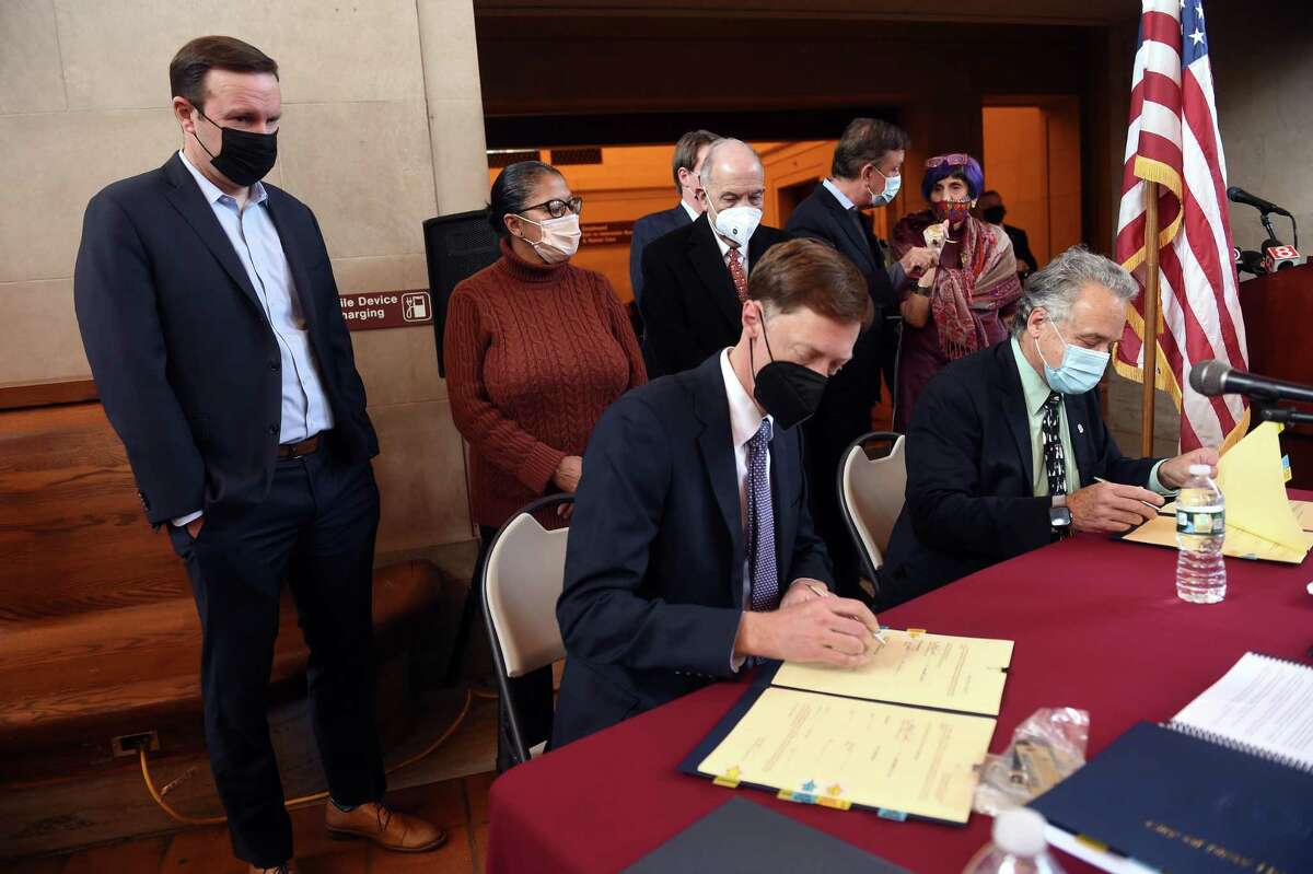 U.S. Sen. Chris Murphy, left, watches New Haven Mayor Justin Elicker, center, and state Department of Transportation Commissioner Joseph Giulietti, right, sign a lease for a partnership agreement for Union Station and State Street Station in New Haven Dec. 21, 2021.