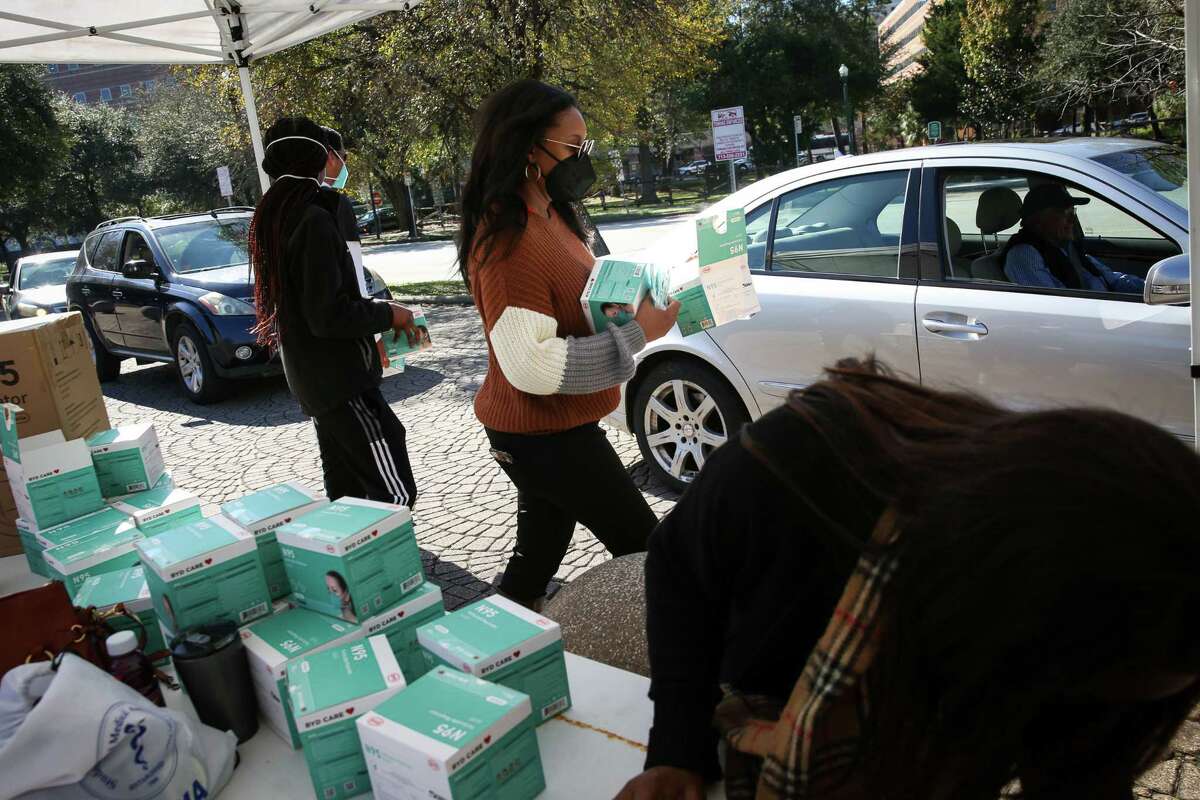 Dr. Brianna Wapples, an emergency medicine physcian, center, helps handout N95 masks to people Tuesday, Dec. 21, 2021, at the Houston Zoo in Houston.