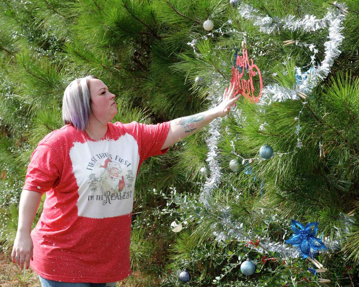 Casey Campbell decorates a tree along FM 1484, Friday, Dec. 17, 2021, in Conroe. Campbell and her family decorated their tree this year to honor her mother who loved Christmas. Residents who live along the road started decorating trees that dotted the thoroughfare two years ago.