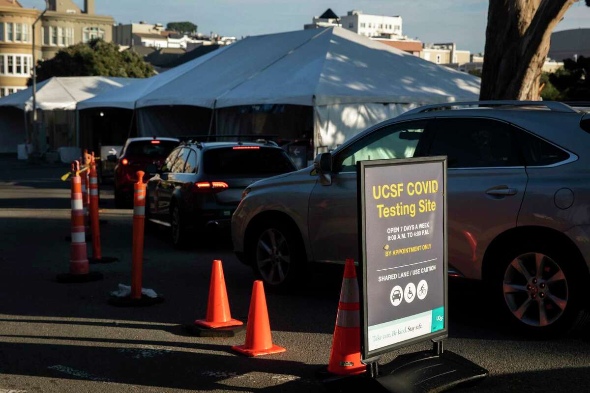 Cars line up to receive a drive-thru COVID-19 test at a site at UCSF’ss Laurel Heights campus in San Francisco on Tuesday. Local health officials are yet again beefing up staff and capacity at testing sites as the omicron wave arrives.