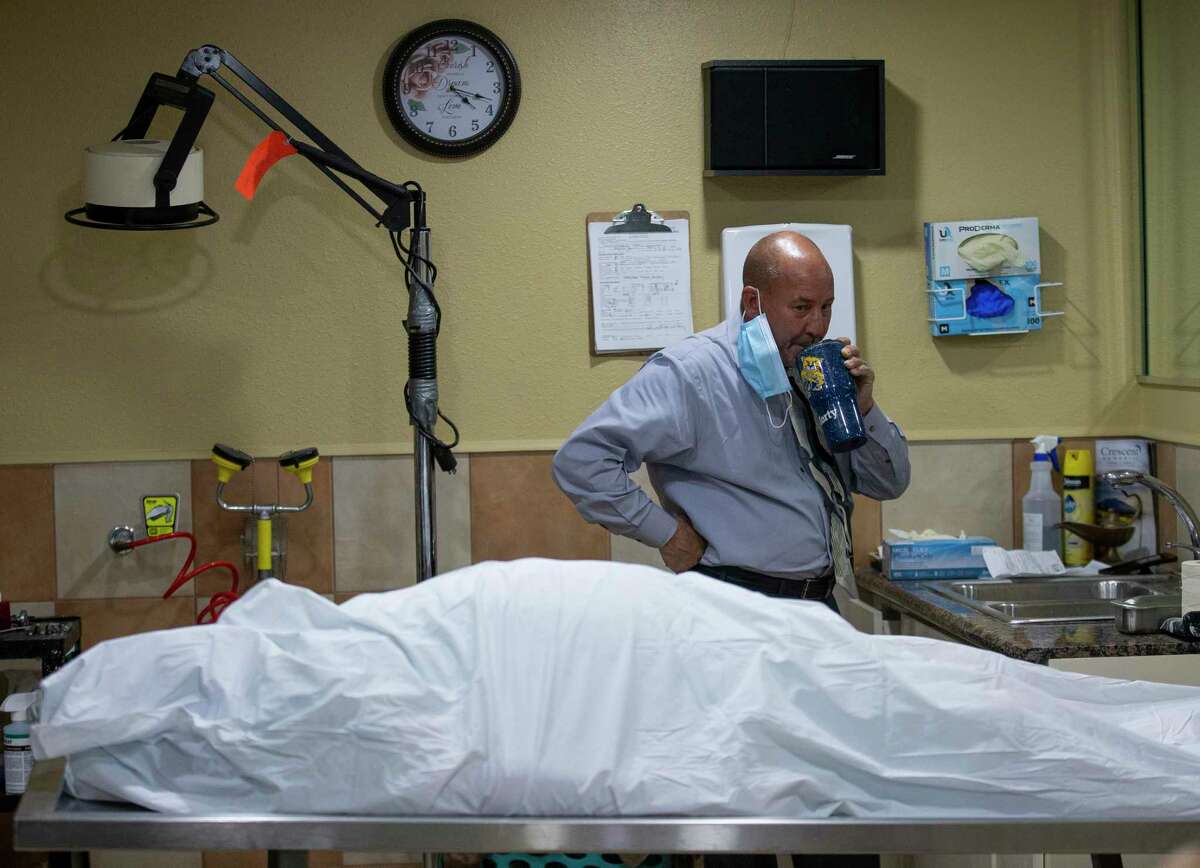 Mortician Jeff Sonka, center, takes a sip of water before starting the third embalment of the day inside the mortuary room at Compean Funeral Home Tuesday, Aug. 4, 2020, in Houston. The funeral home, which serves the Latin community predominantly, has seen its workload double since the pandemic began.