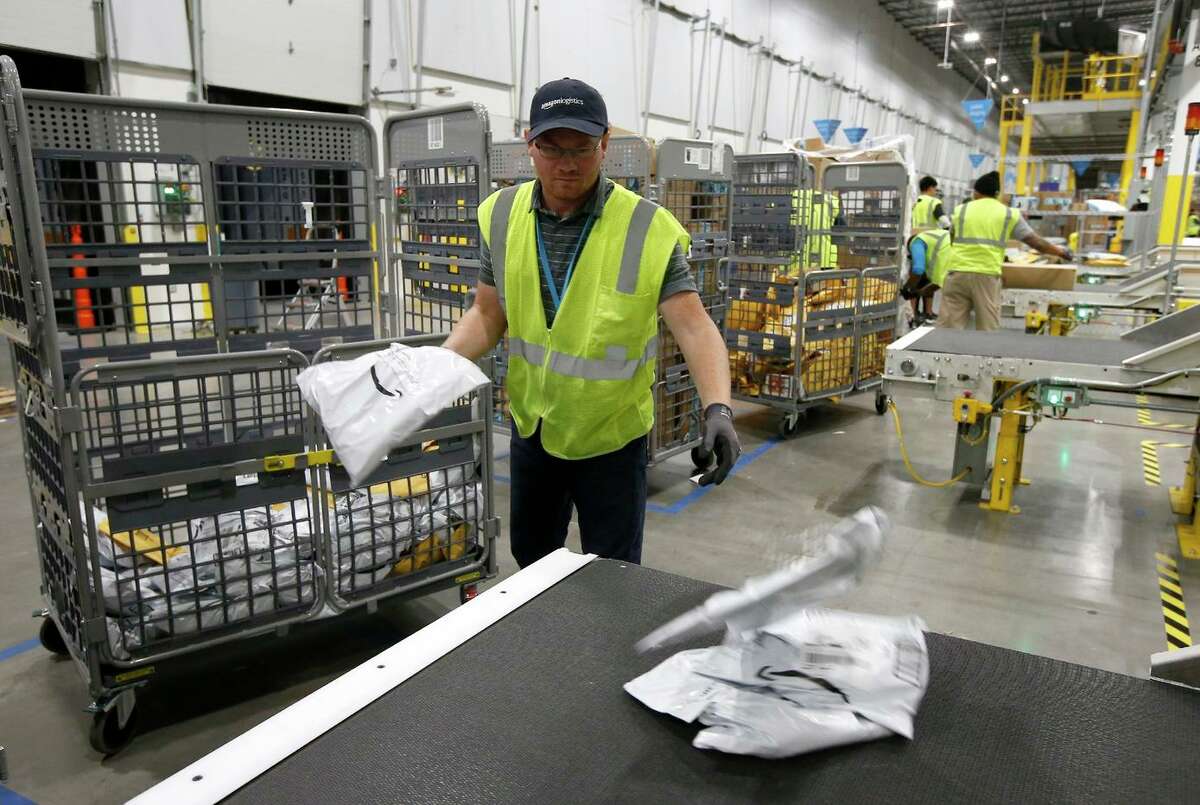Steven Smith places packages onto a conveyor prior to Amazon robots transporting packages to chutes that are organized by ZIP code, at an Amazon warehouse facility in Goodyear, Ariz. on Dec. 17, 2019.