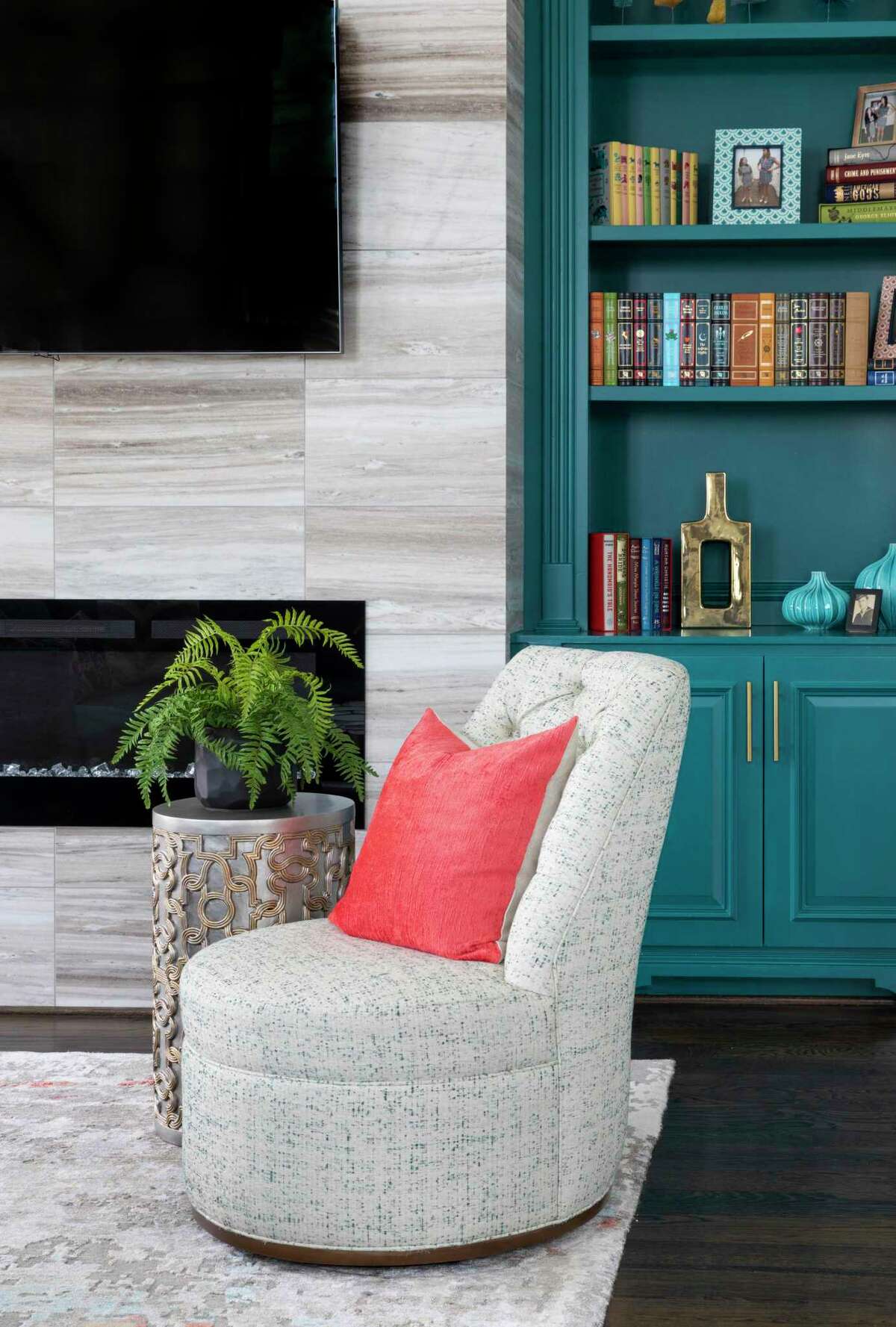 Curved or rounded furniture and bold colors will be a popular trend in homes in 2022, says Pamela O'Brien of Pamela Hope Designs, an interior designer based in Houston.  In this house there is a round swivel chair in front of a light blue-green lacquered bookcase.