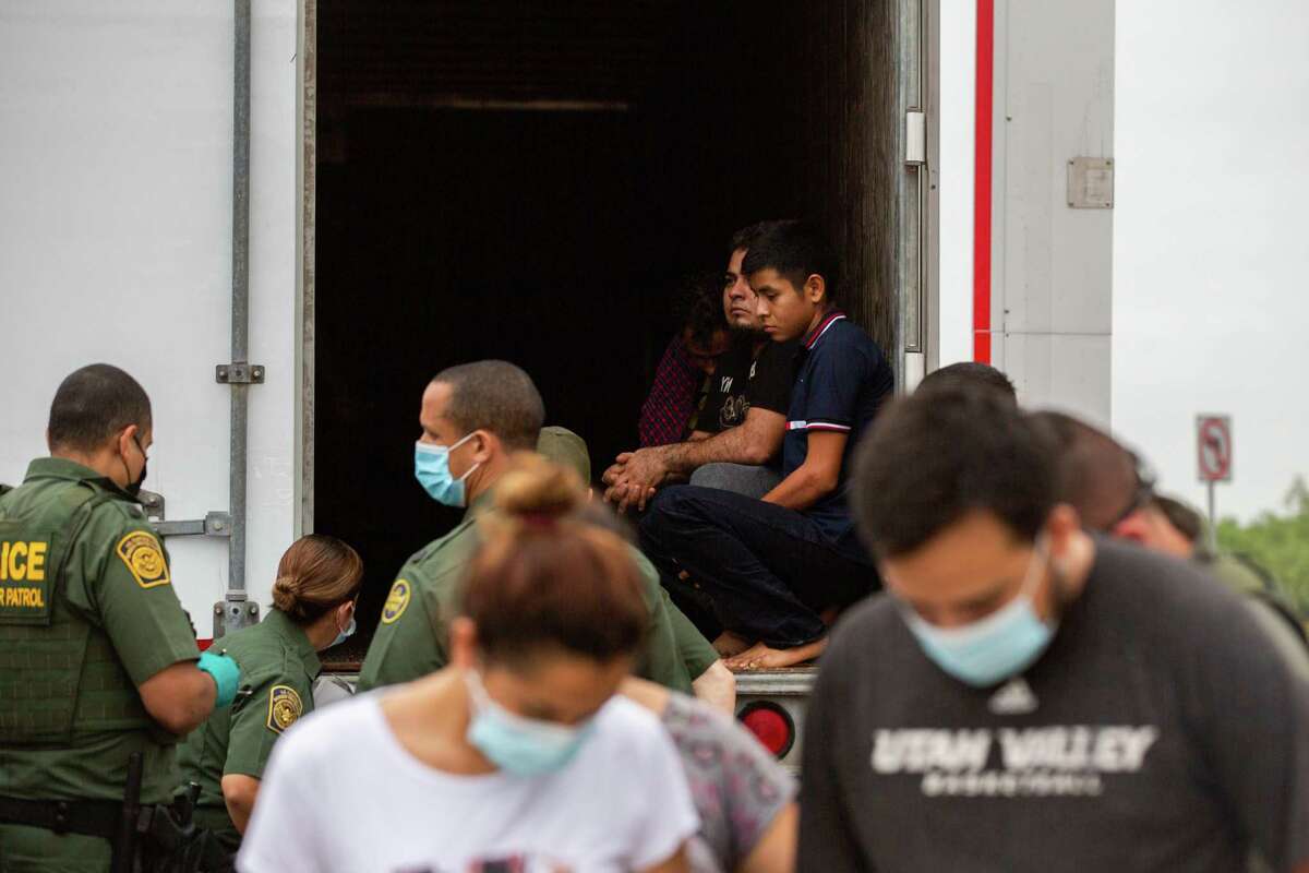 People suspected of crossing the U.S./Mexico border illegally wait for their turn to be handcuffed and given a protective mask as Customs and Border Protection agents process people found inside a trailer at a U.S. Customs and Border Protection inspection station at Interstate 35, Wednesday, May 26, 2021, in Laredo.