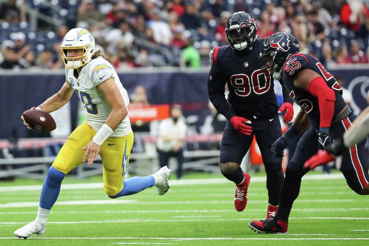 Los Angeles Chargers quarterback Justin Herbert (10) is forced to scramble out of the pocket by Houston Texans defensive end Demarcus Walker and defensive tackle Ross Blacklock (90) during the third quarter of an NFL football game Sunday, Dec. 26, 2021 in Houston.