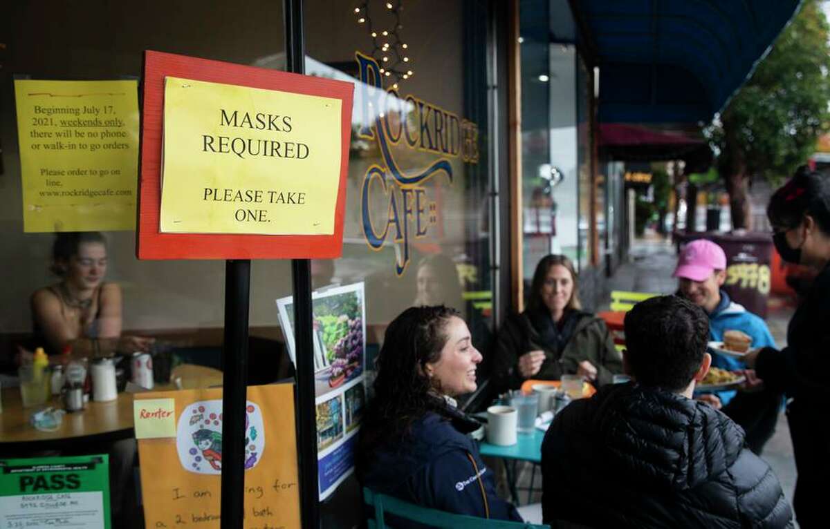 A Rockridge Cafe sign in Oakland informs diners of masking requirements as the latest coronavirus surge sweeps California and the nation.