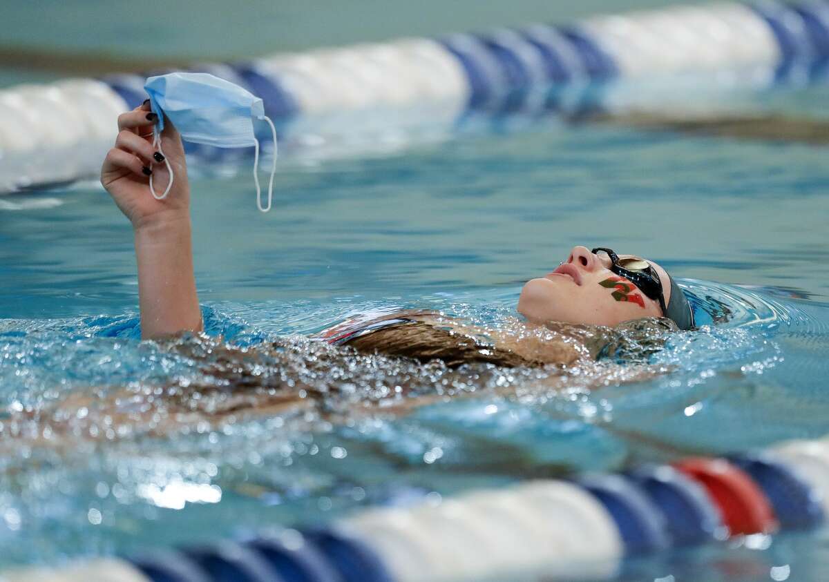 Alyssa Sorensen of The Woodlands holds her mask out of the water as she crosses from one side of the pool to the other before the District 13-6A swimming meet at the Conroe ISD Natatorium, Saturday, Jan. 23, 2021, in Shenandoah.