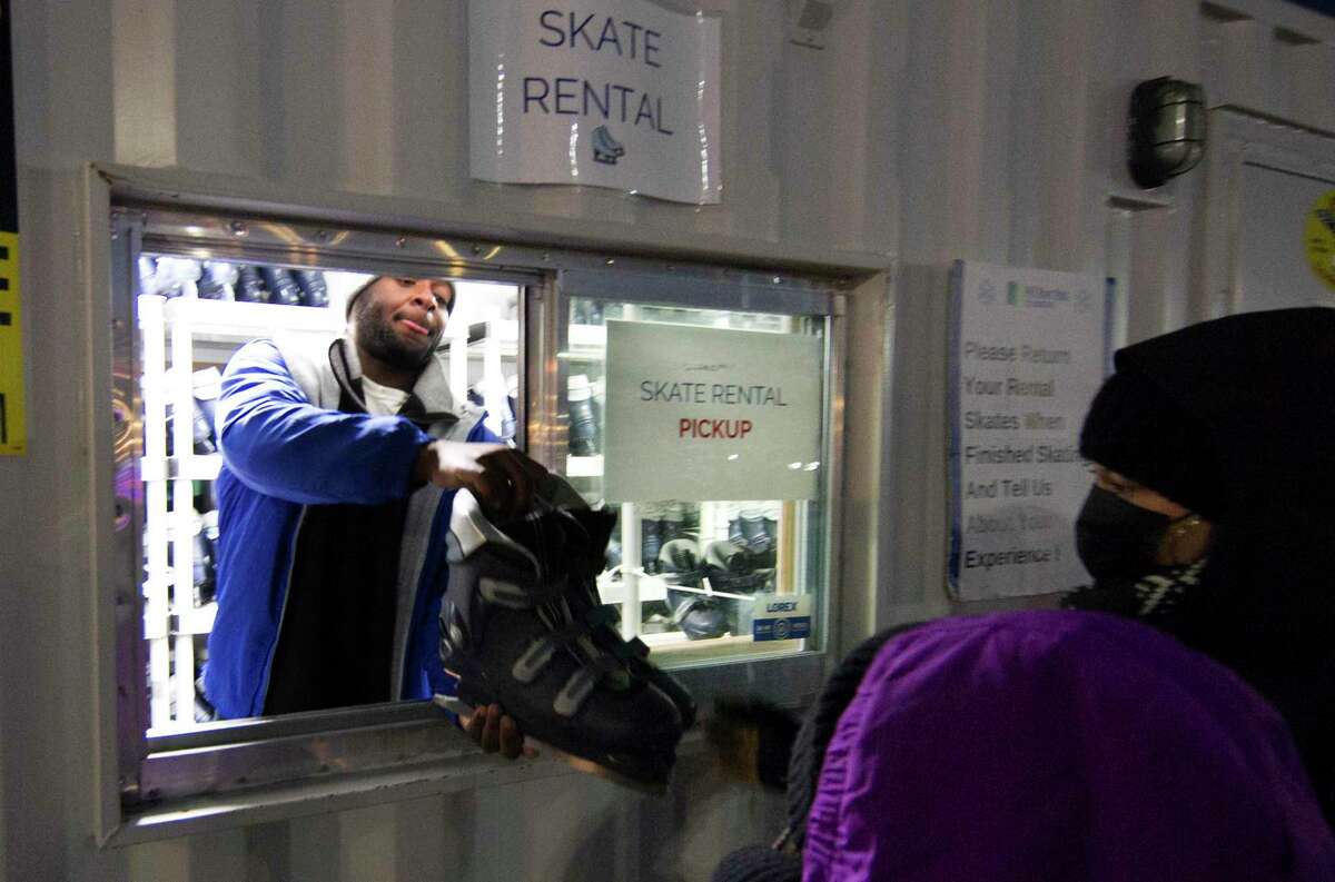 Ross Nazaire, Assist Manager with Ice Rink Events, hands a pair of skates out as area residents gather to enjoy some holiday ice skating at the Cohen Rink at Mill River Park in Stamford, Conn., on Wednesday December 22, 2021.