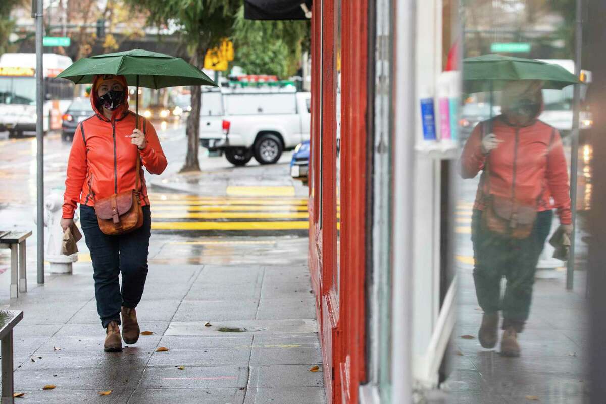 A person carries an umbrella while walking along College Avenue in Oakland, Calif. More rain — and, at higher elevations, snow — was in store for the Bay Area in the coming days. A cold snap could also drop downtown San Francisco to the lowest temperature its seen in years.