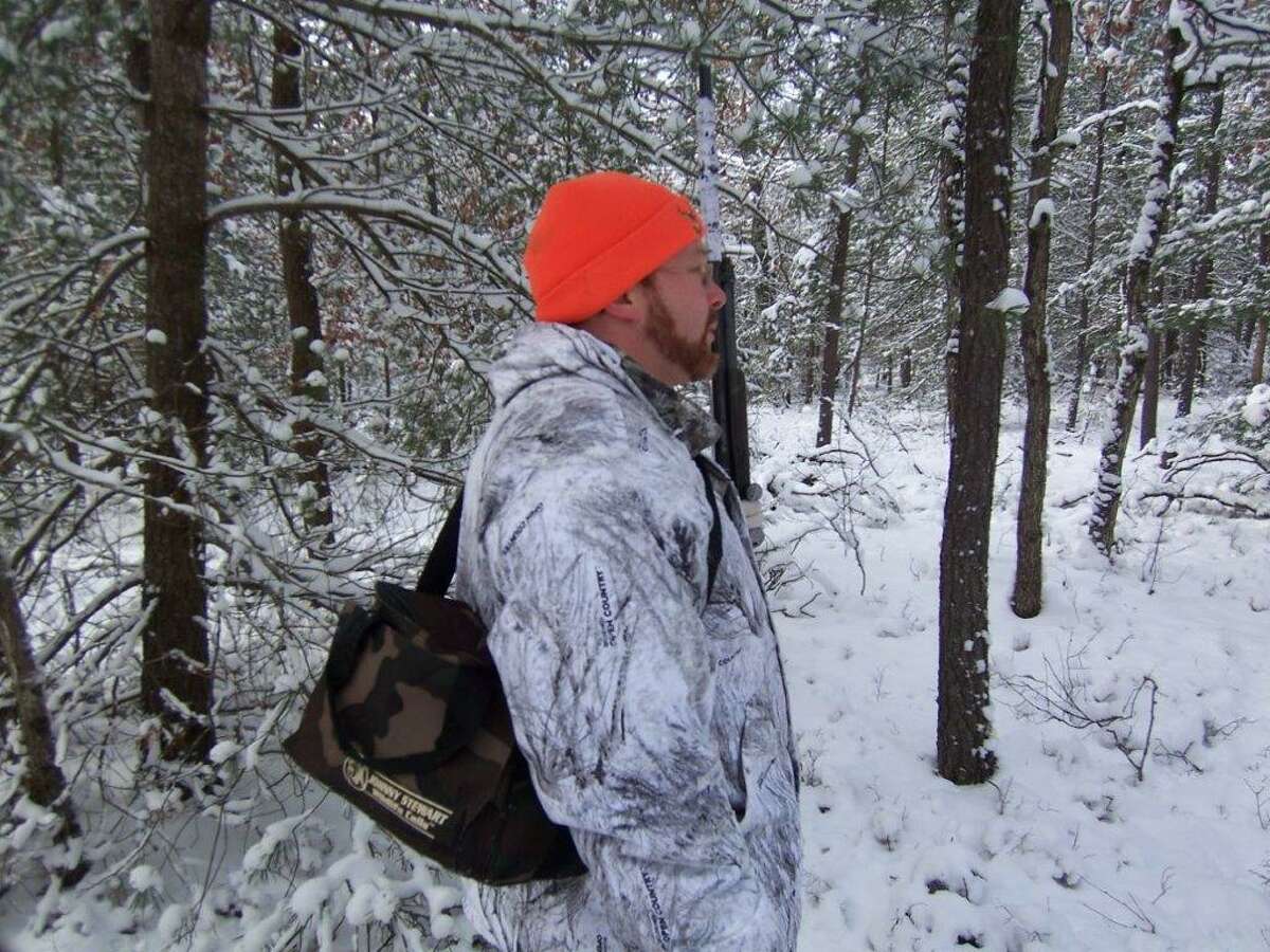 Predator hunter Ryan Walker, of Cass City, with a compact digital caller on his shoulder, picks out the right site to set up in a spot featuring fresh coyote tracks.