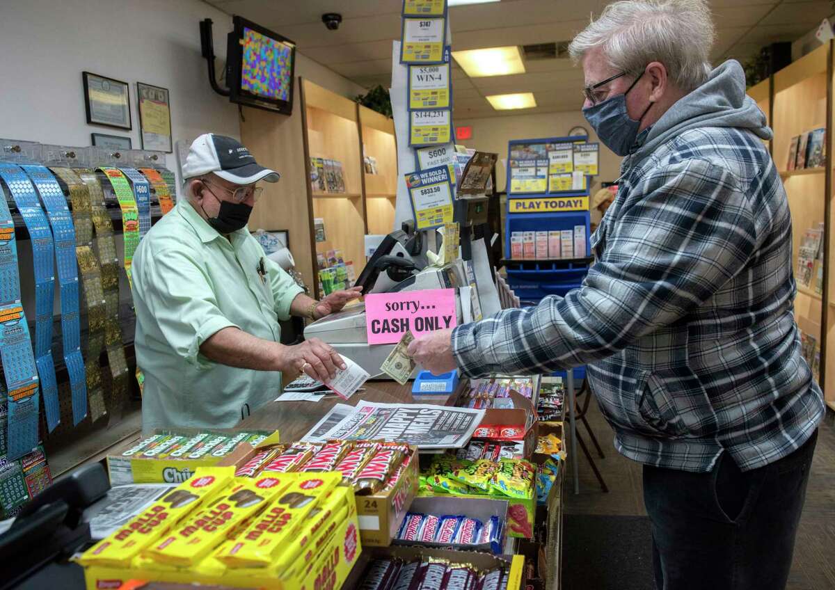 Fershid Hushmendy, owner of Coulson's News and More, sells a Powerball lottery ticket to Tom O’Donnell of Latham on Tuesday, Dec. 28, 2021 in Latham, N.Y. The Powerball jackpot is now $441 million.
