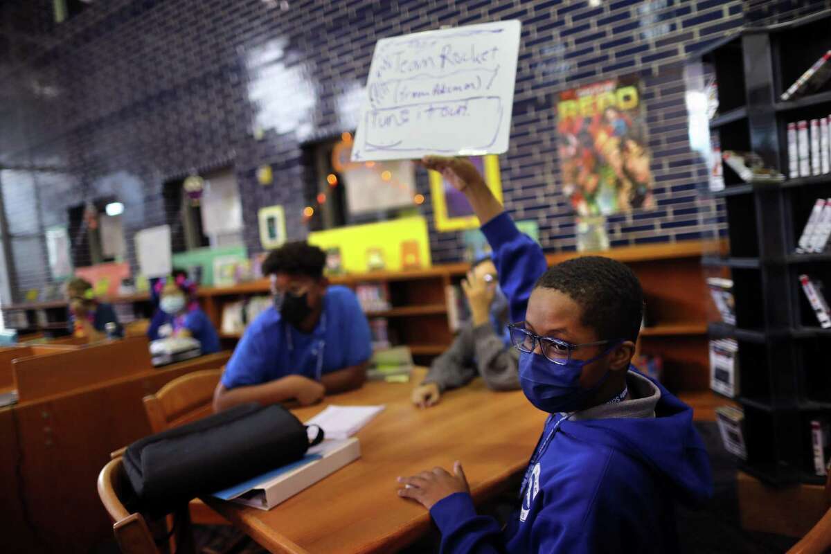 Pin Oak Middle School student John Covington, 14, raises a white board with the title of a book during a Name That Book competition at the library of the school, Thursday, Oct. 14, 2021, in Houston.