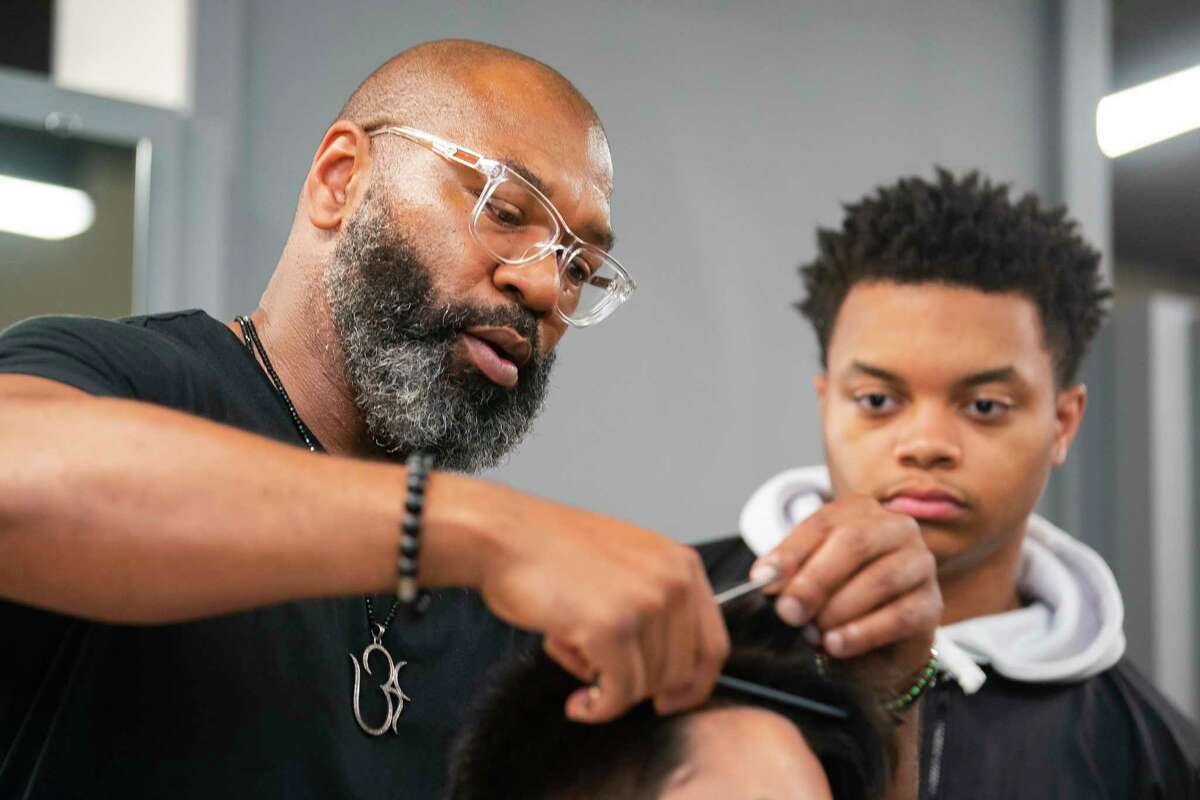 Barbering instructor Eros Shaw demonstrates how he wants Doreoni Smith, 16, to cut classmate Jacob Lara’s hair during class inside the newly built barbering academy, Tuesday, Dec. 7, 2021, at Westfield High School in Houston.