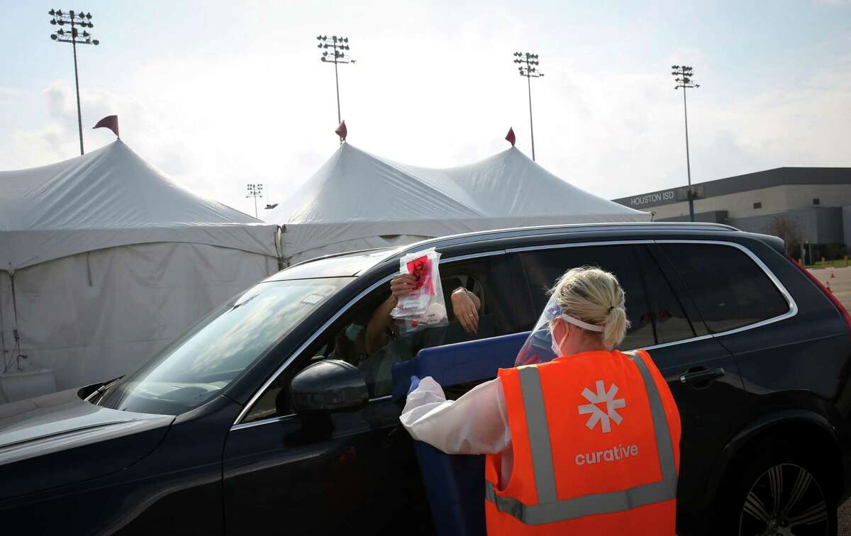 Emma Vaughn, a site lead, collects COVID-19 test packets from a person after a group of people in a vehicle took the tests Wednesday, Dec. 29, 2021, at Delmar Stadium in Houston. The Houston Health Department and Curative opened the drive-thru mega-site that morning.