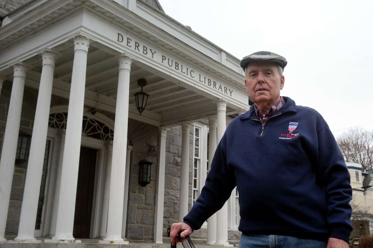 Jack Walsh, former head of the Derby Historical Society, poses in front of the Derby Public Library, in Derby, Conn. Dec. 29, 2021. Walsh has created the Historic Birmingham Borough District Map, an online interactive map including many points of historic interest around Derby, Connecticut’s smallest city, including the Derby Public Library, built in 1912.