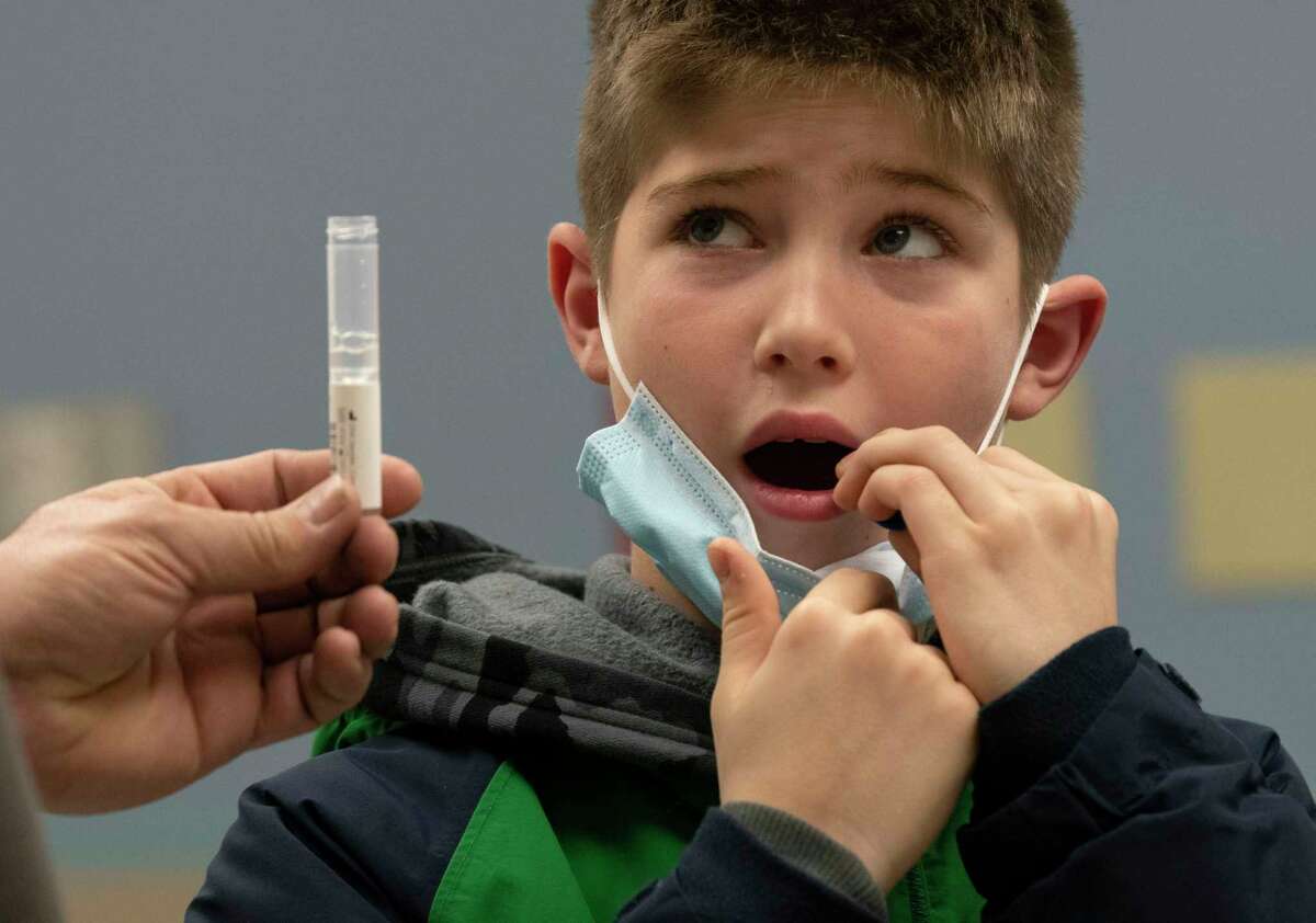 Chris Mills of Scotia holds the test tube for his son William Mills, 10, while he swabs the inside of his mouth as he gets tested for COVID-19 at the Schenectady County community COVID testing site on Tuesday, Jan. 4, 2022 in Schenectady, N.Y. Rates of COVID-19 infection among schools exploded over the holiday break.