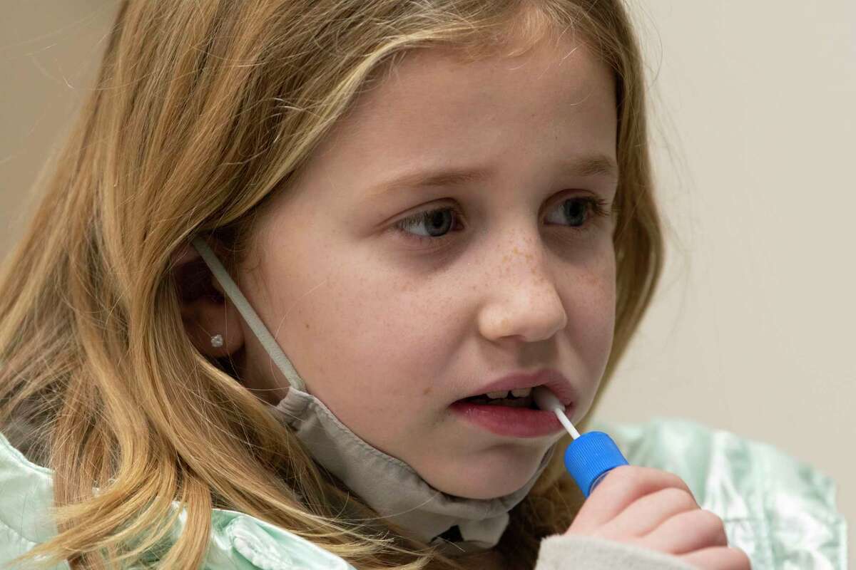 Emily Piazza, 7, of Glenville swabs the inside of her mouth as she gets tested for COVID-19 at the Schenectady County community COVID testing site on Tuesday, Jan. 4, 2022 in Schenectady, N.Y.