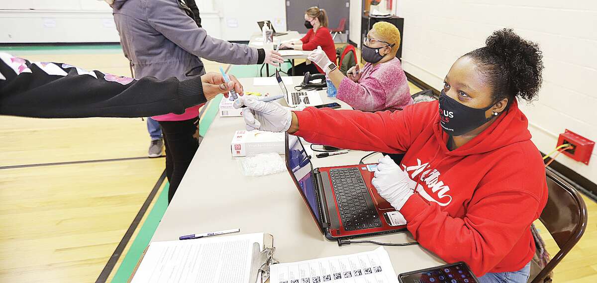 John Badman|The Telegraph Employees of Med-Call Healthcare, Inc., right, based in Warrenville, Illinois, handle tests and paperwork Tuesday for COVID-19 testing at North Elementary School in Godfrey. Alton school district students will return from the holiday break on Wednesday.