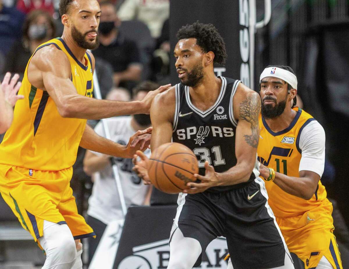 Spurs forward Keita Bates-Diop dishes to the outside while being defended by Jazz center Rudy Gobert, left, and Jazz forward Mike Conley on Monday, Dec. 27, 2021, the AT&T Center.