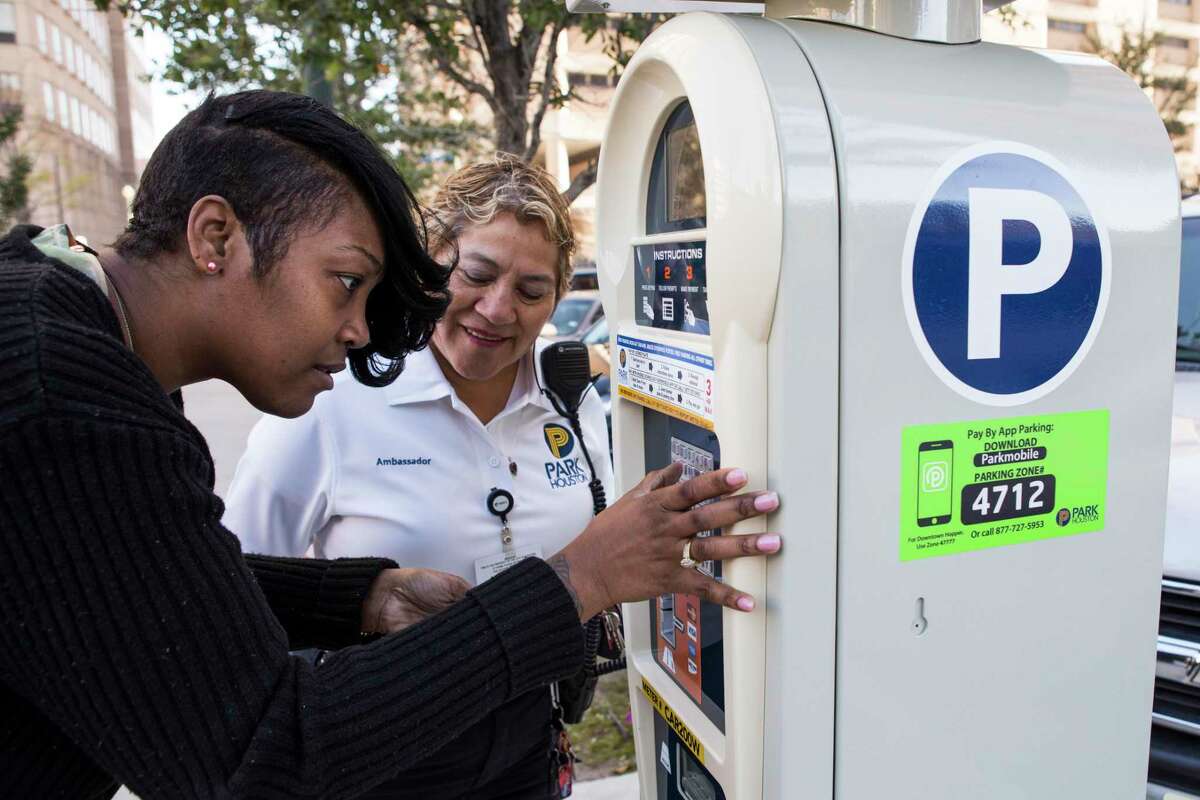 Tyra Brown uses one of the city's new parking meters as Olga Valdez, parking compliance officer, stands by on Feb. 16, 2016, in Houston. The city is warning users not to trust QR codes if they see them on the sides of meters.