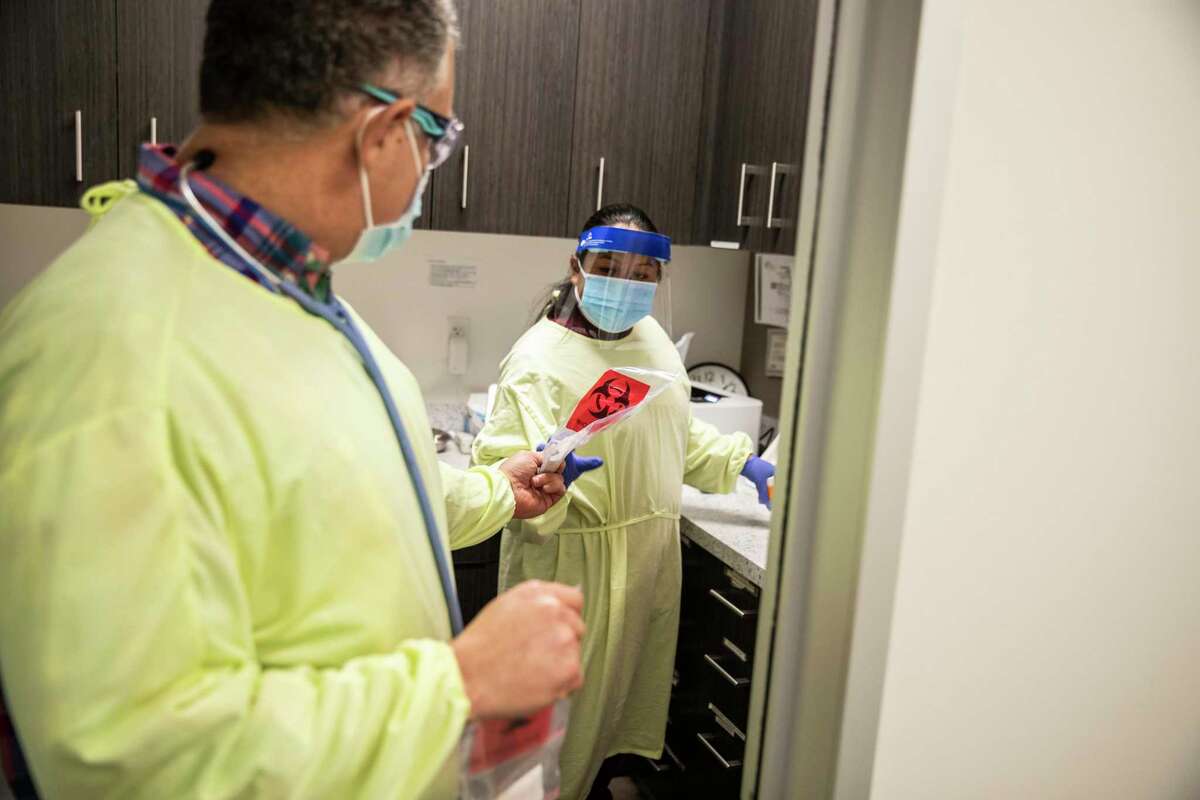 在加州旧金山金门儿科，约书亚·帕克医生(左)将新冠病毒检测样本递给医疗助理凯瑟琳·皮内达。