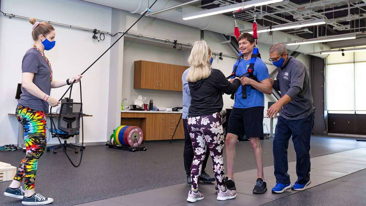 Sean Carter practices walking in a harness, guided by Health and Human Performance Institute clinical director Dr. Joe Hazzard, right, and graduate students in University of Houston-Clear Lake’s exercise sciences program.