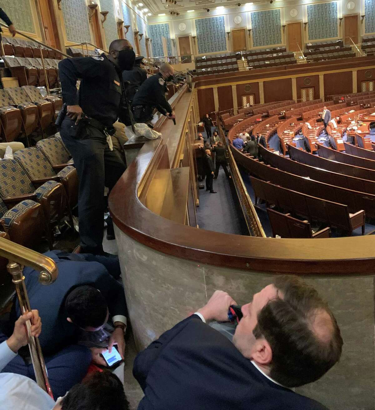 U.S. Rep. Jason Crow, at bottom, a Colorado Democrat, crouches under the rail of the gallery in the U.S. House of Representatives chamber on Jan. 6, 2021.