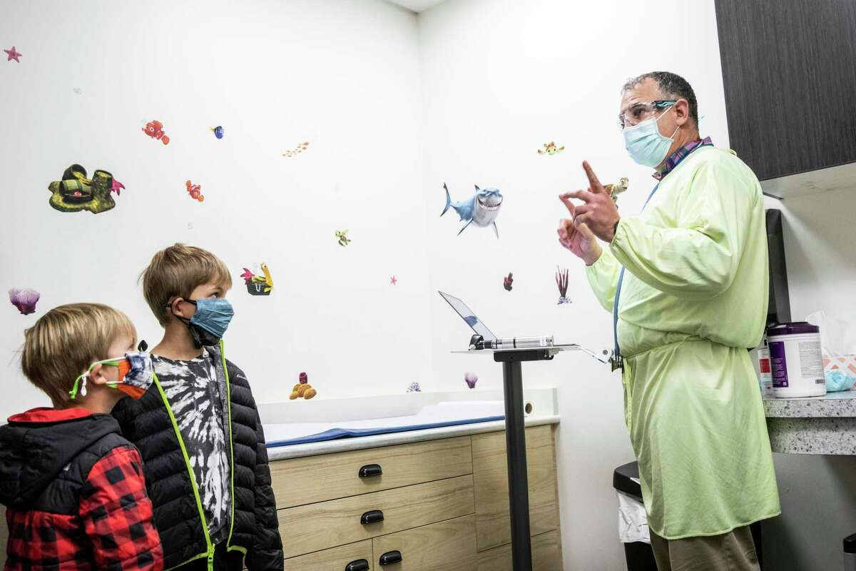 Dr. Joshua Parker, right, explains the COVID-19 PCR test as Tucker Brady, 4, left, and brother Jimmy, 6 at Golden Gate Pediatrics in San Francisco, Calif.