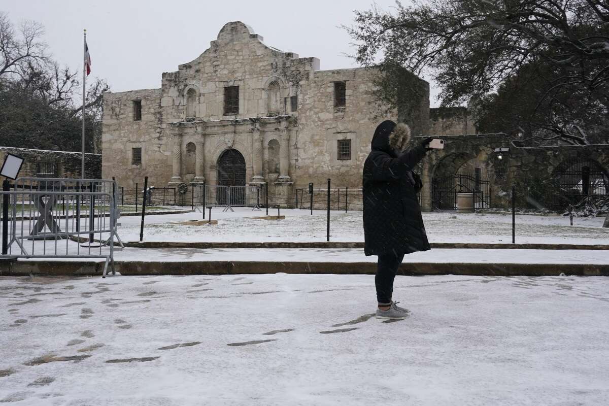 A woman takes a selfie as snow falls over the Alamo, Thursday, Feb. 18, 2021, in San Antonio. Snow, ice and sub-freezing weather continue to wreak havoc on the state's power grid and utilities. (AP Photo/Eric Gay)