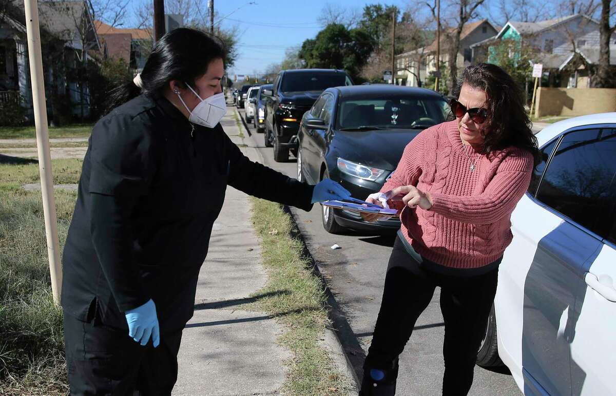 A screener hands Andreana Perez, right, paperwork for a COVID test. Motorists seeking tests lined the streets around Woodlawn Avenue and Zarzamora Street.