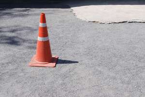 Traffic cone, with white and orange stripes on road.
