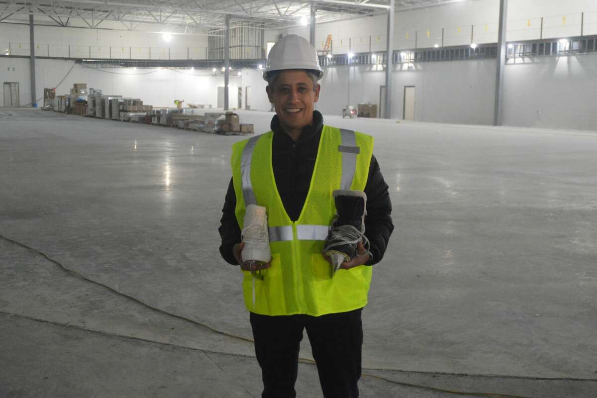 R.P. Lumber Center Superintendent Phil Zamora poses with a figure ice skate and a hockey skate. Behind him is the ongoing construction of the new ice rink on Tiger Drive. 